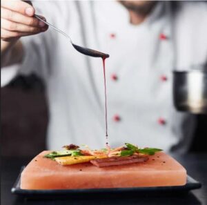 Professional chef demonstrating proper grilling techniques on a pink Himalayan salt block