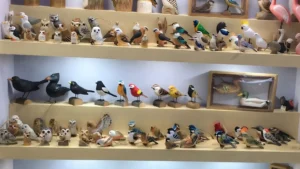 A showroom shelf display featuring a diverse collection of wholesale hand-carved basswood and pine wooden bird figurines, showcasing retail-ready artisan crafts for B2B buyers.