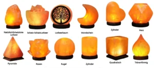 A collection of hand-carved Himalayan pink salt lamps in various shapes including pyramid, sphere, heart, crescent moon, cylinder, and an intricate Tree of Life relief carving on rosewood bases.