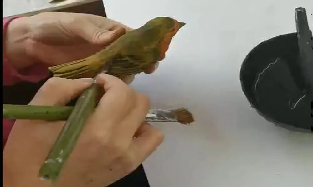 Artisan hand-painting feather details on a wooden robin bird at the factory