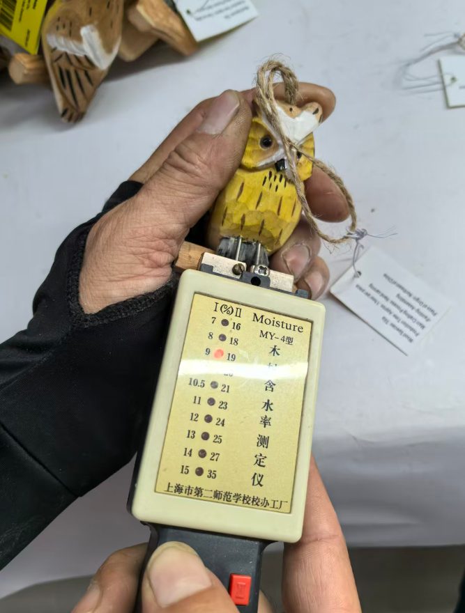 QC worker measuring moisture content of hand-carved wooden owl keychain