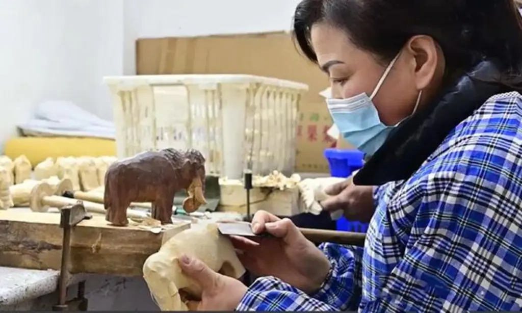 Batch consistency in practice: An artisan meticulously shapes a raw wooden piece while strictly referencing the approved master sample (left) to ensure uniform dimensions and details across the entire production run