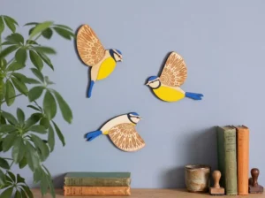 Three-piece hand-carved wooden blue tit flying birds wall art set with intricate laser-engraved wings mounted on a boutique feature wall