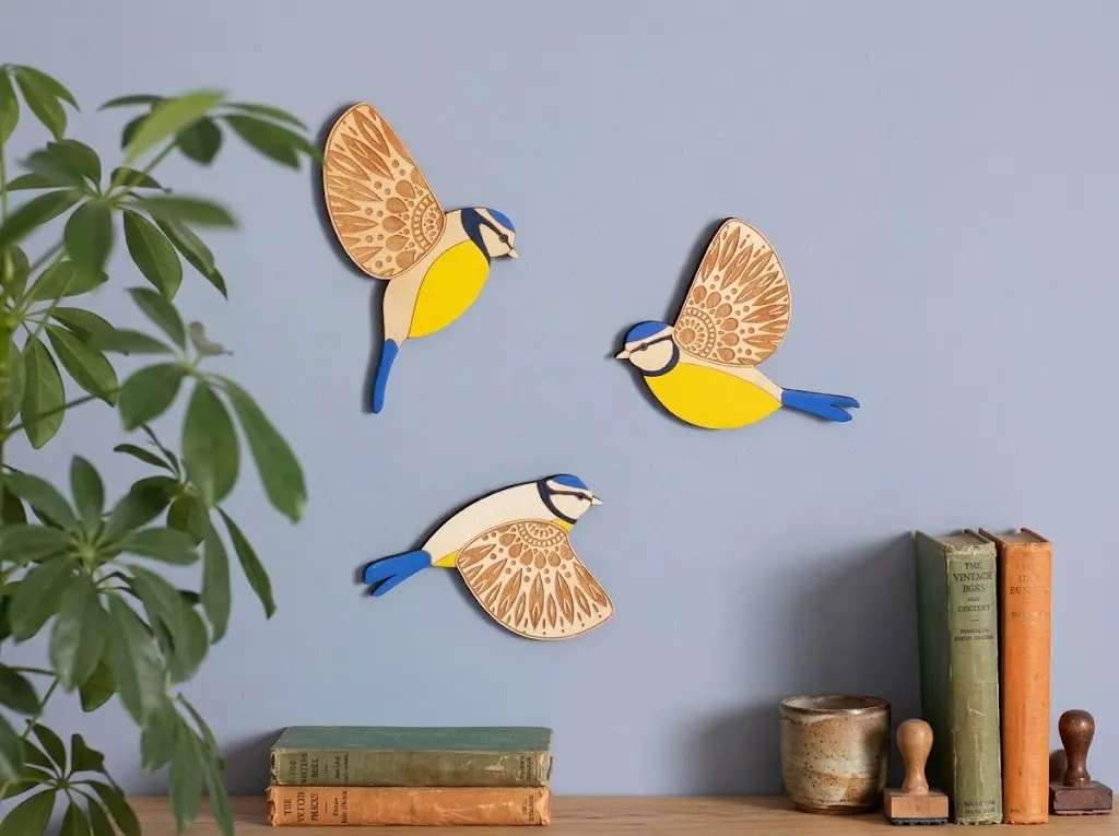 Three-piece hand-carved wooden blue tit flying birds wall art set with intricate laser-engraved wings mounted on a boutique feature wall